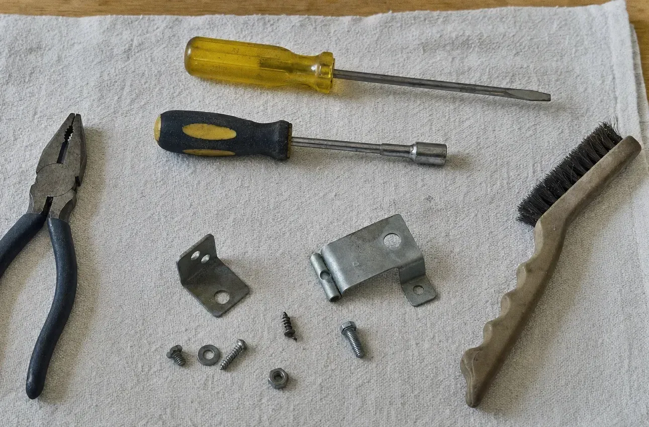 A screwdriver and a nut driver laid on a cloth beside two steel brackets, loose screws and a small spring